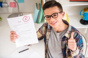 A happy high school boy holding up a paper with an "A+" on it.